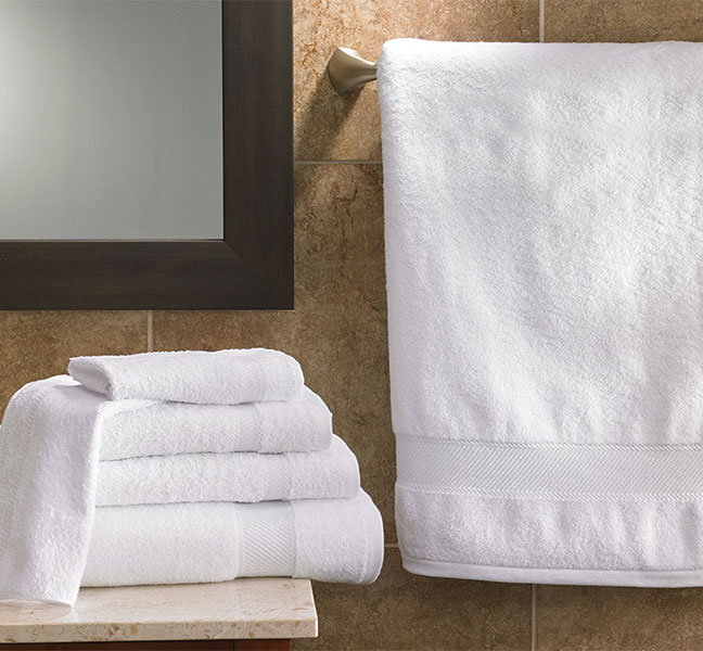 Four different sized towels stacked on top of a sink and an extended robe on the right of the image
