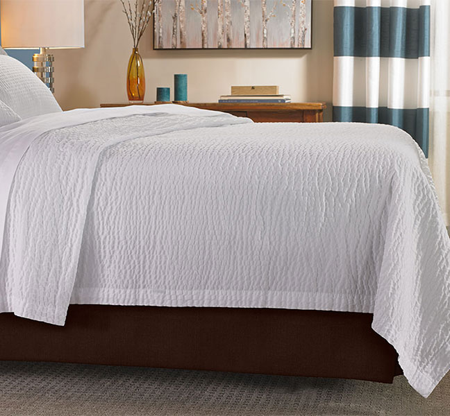 White rippled coverlet on top of a brown bed