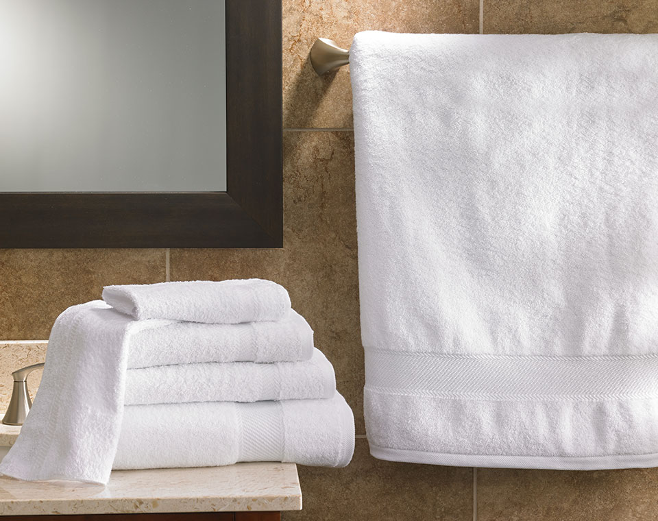 Four different sized towels stacked on top of a sink and an extended robe on the right of the image